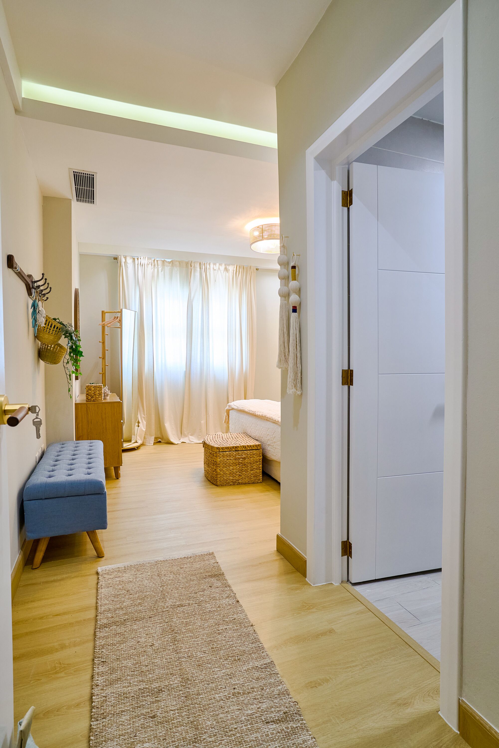 A room with a bed, a bench, a wardrobe, a mirror, and a door.