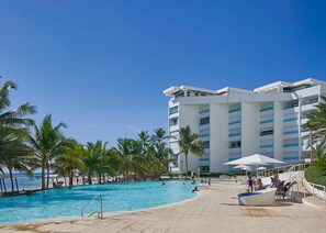 A hotel with a swimming pool, palm trees, and a beach in the background. - Marbella LUX Sunsets Beachfront Pool Families (Guayacanes)