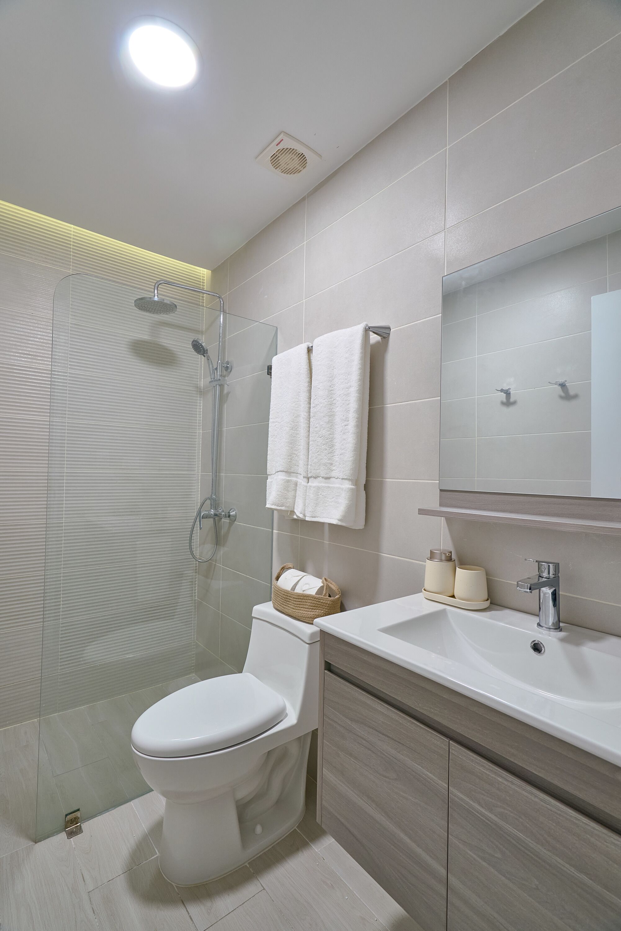 A modern bathroom with a glass shower enclosure, a white toilet, a vanity with a mirror, and a towel rack.