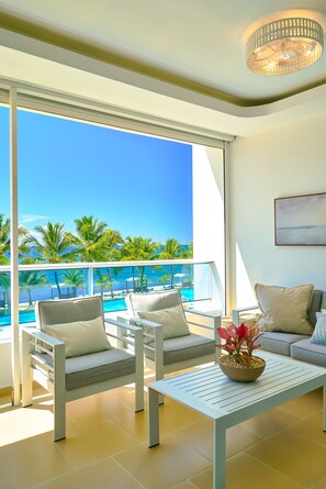 A balcony with a view of a pool and palm trees, a sofa, and a table with a plant. - Marbella LUX Sunsets Beachfront Pool Families (Guayacanes)