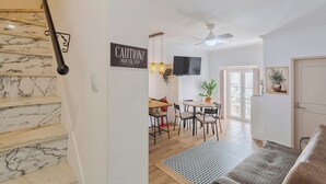 A staircase with marble steps, a caution sign, a dining area with a table and chairs, a ceiling fan, and a door. - Duplex Postigo da Pedra (Setúbal)