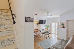 A staircase with marble steps, a caution sign, a dining area with a table and chairs, a ceiling fan, and a door. - Duplex Postigo da Pedra (Setúbal)