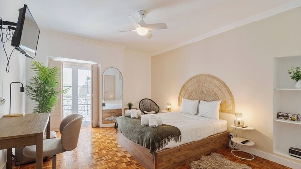A bedroom with a wooden bed, a desk, a chair, a ceiling fan, and a plant. - Duplex Postigo da Pedra (Setúbal)