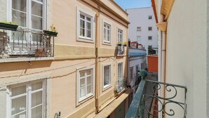A narrow urban street with multi-story buildings, balconies with railings, and visible windows. - Duplex Postigo da Pedra (Setúbal)