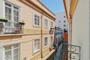 A narrow urban street with multi-story buildings, balconies with railings, and visible windows. - Duplex Postigo da Pedra (Setúbal)