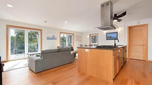 A modern kitchen with a central island, a dining area with a sofa, and large windows offering a view of the outdoors.