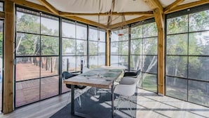 A tented room with a table and chairs, large windows, and a view of the outdoors.