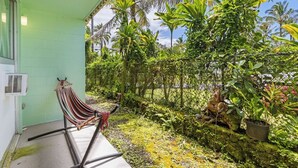 A hammock on a porch with a lush tropical garden and a chain-link fence. - Private Balcony • Walk to Beach + Downtown (Hilo)