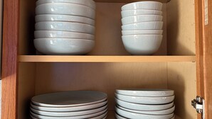 Un mueble de madera con dos estantes, cada uno con pilas de platos de cerámica blanca.
