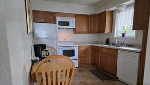 Una cocina compacta con gabinetes de madera, un refrigerador blanco, una estufa, un microondas y un lavavajillas.