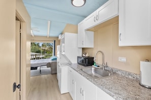 Una cocina compacta con gabinetes blancos, encimera de granito, lavamanos y microondas.