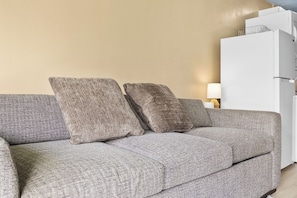 Un sofá gris con dos almohadas, un armario blanco y una lámpara sobre una pared color beige.