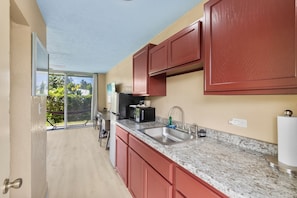 Una cocina con un ventanal grande, un lavabo, un refrigerador y un microondas.