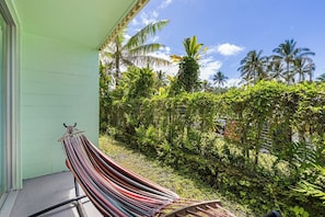 A hammock on a porch with a view of lush greenery and palm trees.