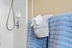 A bathroom with a shower, a towel rack with a blue towel and a white towel.