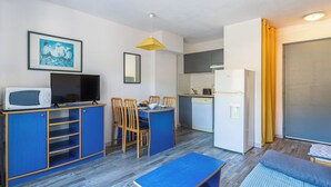 Un espacio habitable compacto con kitchenette, comedor, televisor y cama.