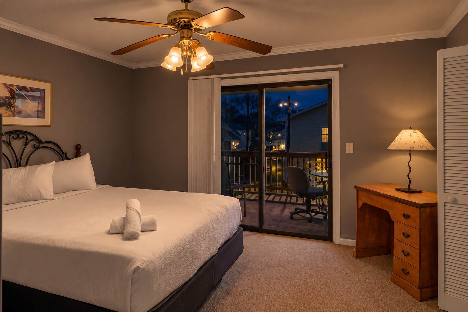 A bedroom with a bed, a ceiling fan, a nightstand, and a view of the outside.
