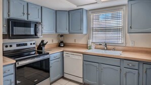 Une cuisine compacte équipée d’un four à micro-ondes, d’une cuisinière, d’un lave-vaisselle et d’une fenêtre avec des stores.