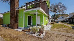 Une maison à deux étages, avec une façade verte, une cheminée en briques et un porche avant couvert.