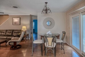 A living room with a leather sofa, a round dining table with chairs, a lamp, and a chandelier.
