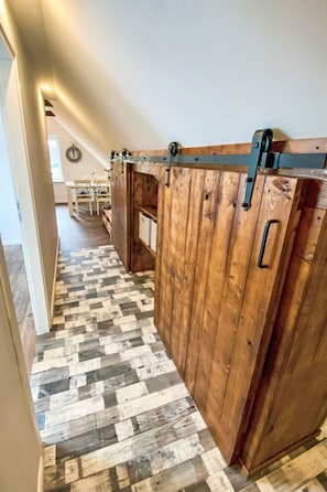 A hallway with wooden flooring, a sliding barn door, and a dining area in the background. - Apartment AHOI by Interhome (Norddeich (Dithmarschen))