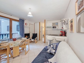 A living room with a sofa, a dining table with chairs, a fireplace, a kitchen area with a microwave, and a window with curtains. - Bel Alp by Interhome (Saint Gervais)