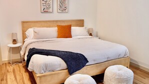 A bed with a wooden frame, white bedding, and two white poufs. - Fully Remodeled & Newly Furnished Browne's Addition Condo - Dog Friendly! (Spokane)