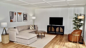 A modern living room with a sectional sofa, a coffee table, a TV on a black stand, a floor lamp, and a potted plant. - Fully Remodeled & Newly Furnished Browne's Addition Condo - Dog Friendly! (Spokane)