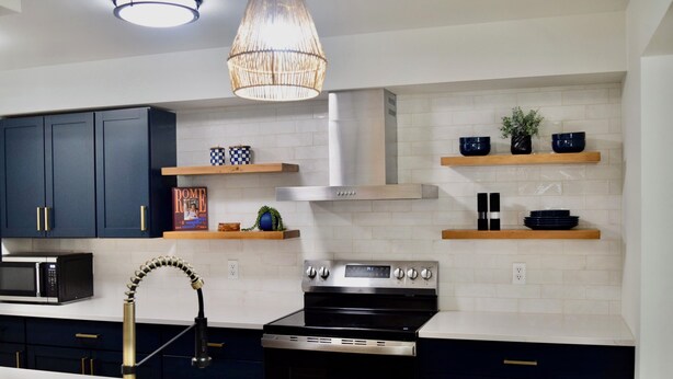A modern kitchen with dark cabinets, a stainless steel stove, a microwave, and a pendant light. - Fully Remodeled & Newly Furnished Browne's Addition Condo - Dog Friendly! (Spokane)