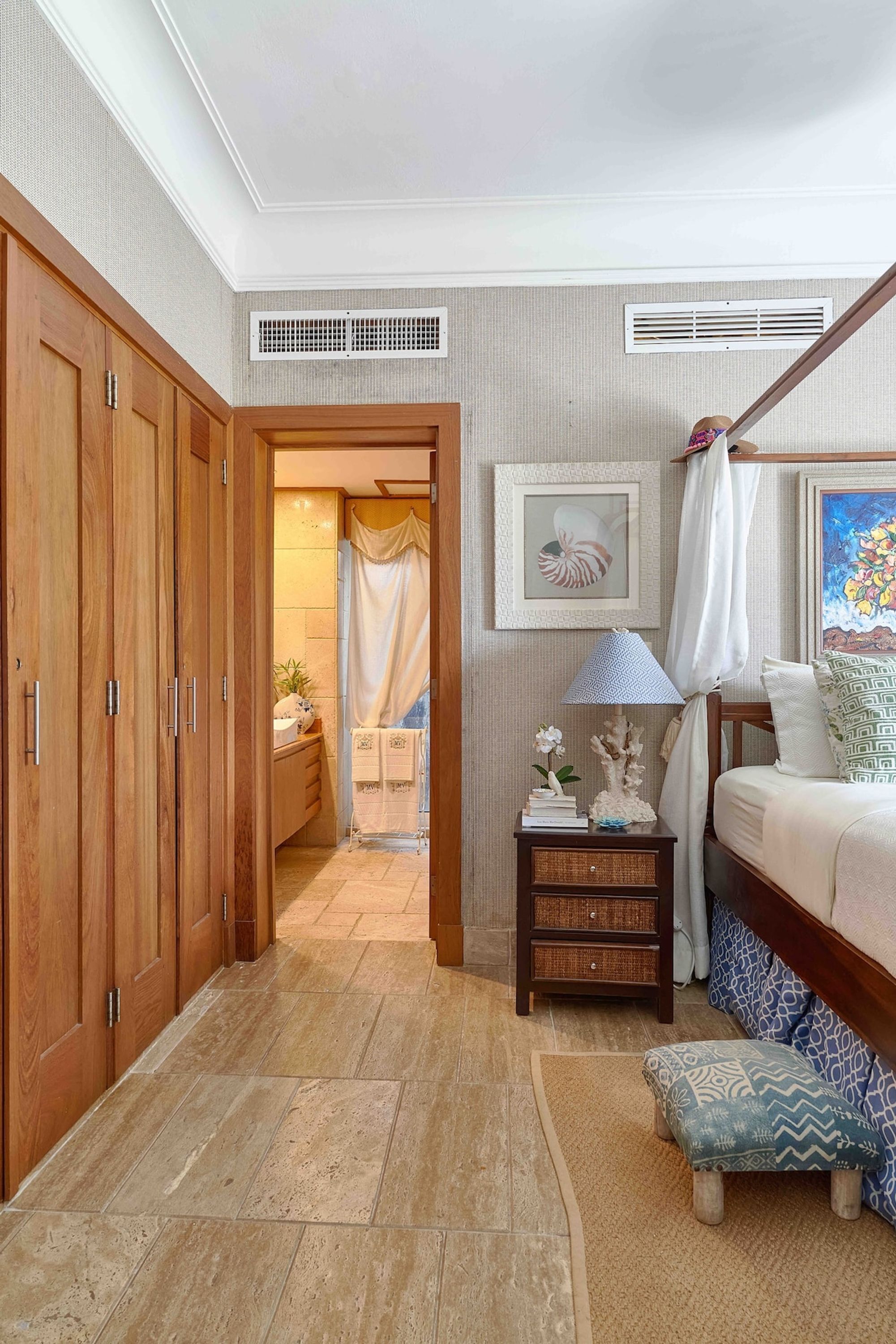A bedroom with a bed, a nightstand, a wooden wardrobe, a bathroom with a shower, and a painting on the wall.