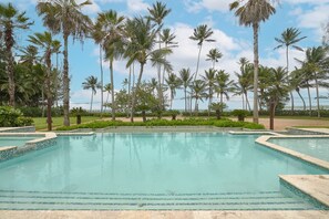 A swimming pool with clear blue water, surrounded by palm trees and a grassy area. - 3BR Beach Essence Terrenas Pool Maid Beachfront (Las Terrenas)