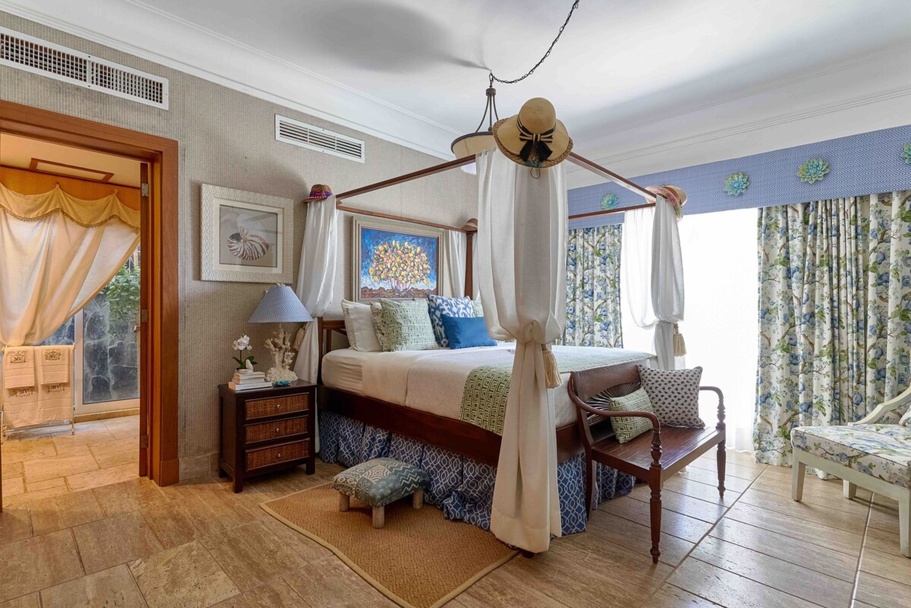 A bedroom with a canopy bed, a wooden nightstand, a chair, and a view of the outdoors.