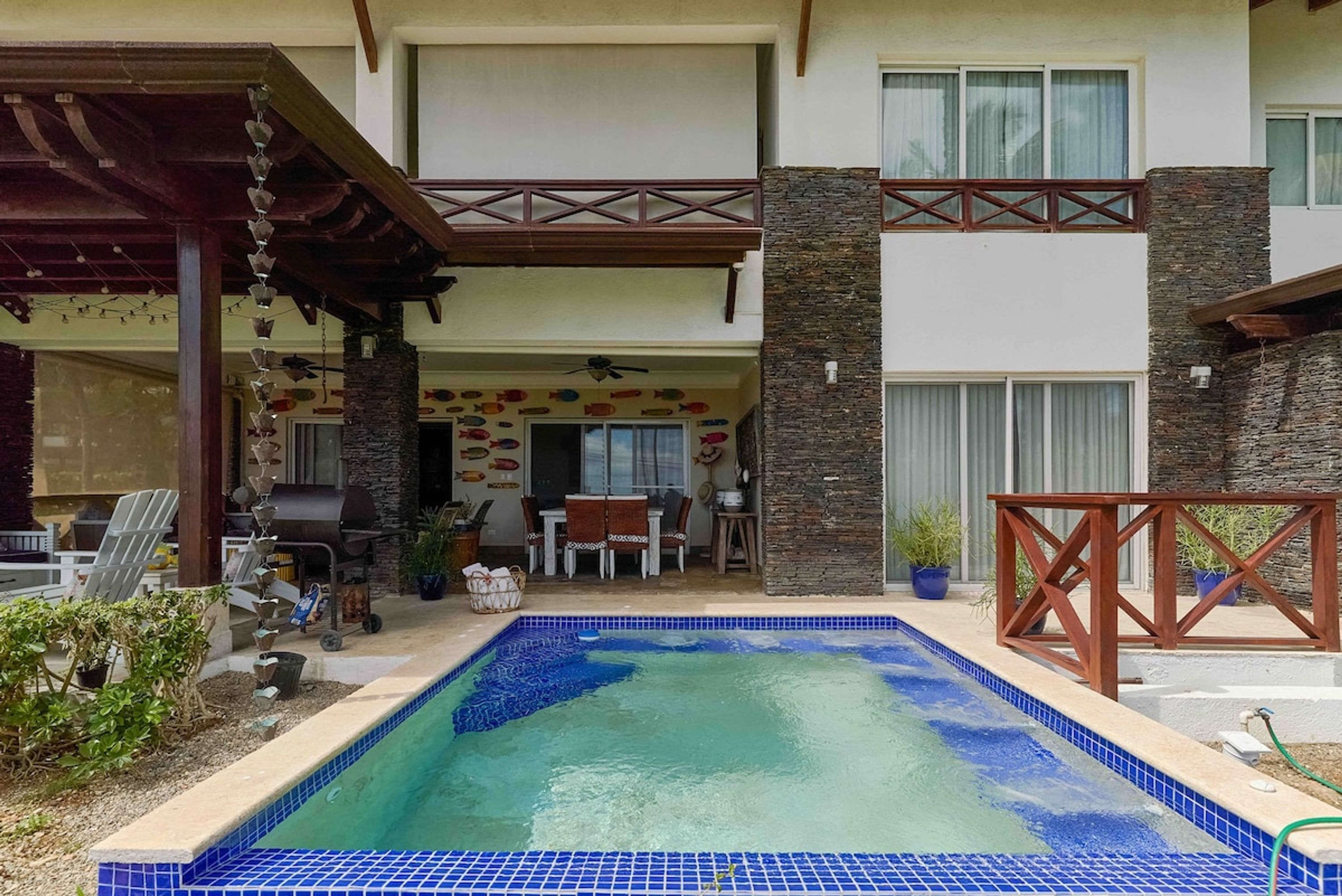 Een huis met twee verdiepingen, een zwembad, buitenmeubels en een barbecueplek.
