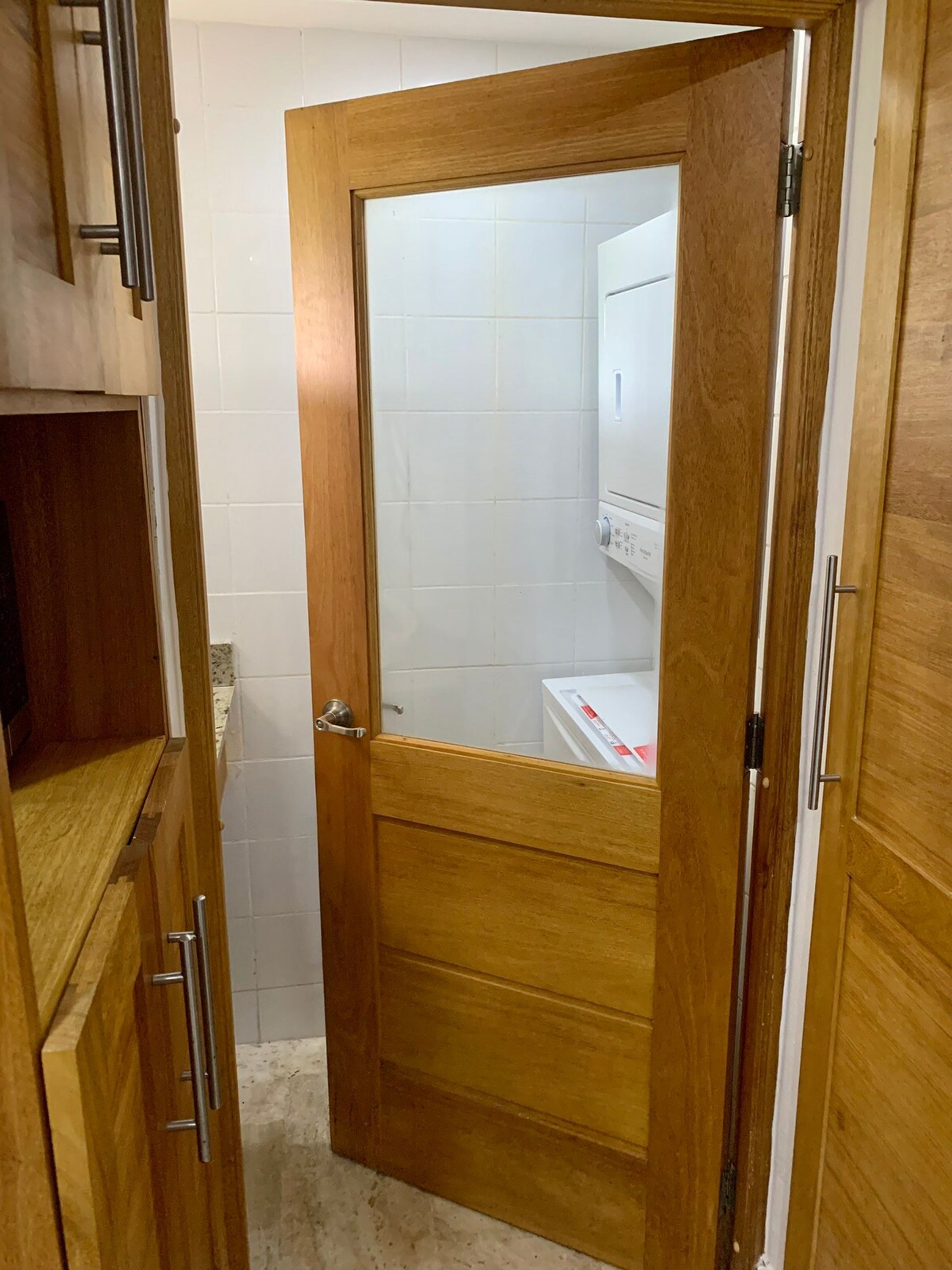 Une porte en bois avec un panneau de verre qui donne sur une salle de bain carrelée de carreaux blancs et équipée de toilettes.