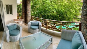 Un balcon agrémenté de meubles en osier, d’une table en verre et offrant une vue sur une piscine.