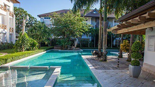Une piscine dotée d’une terrasse carrelée, entourée de verdure et agrémentée d’une pergola.
