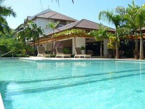 A clear swimming pool with lounge chairs, palm trees, and a building with a tiled roof. - Terrenas Beach Spot Monserrat Pool 5min Beach (Las Terrenas)