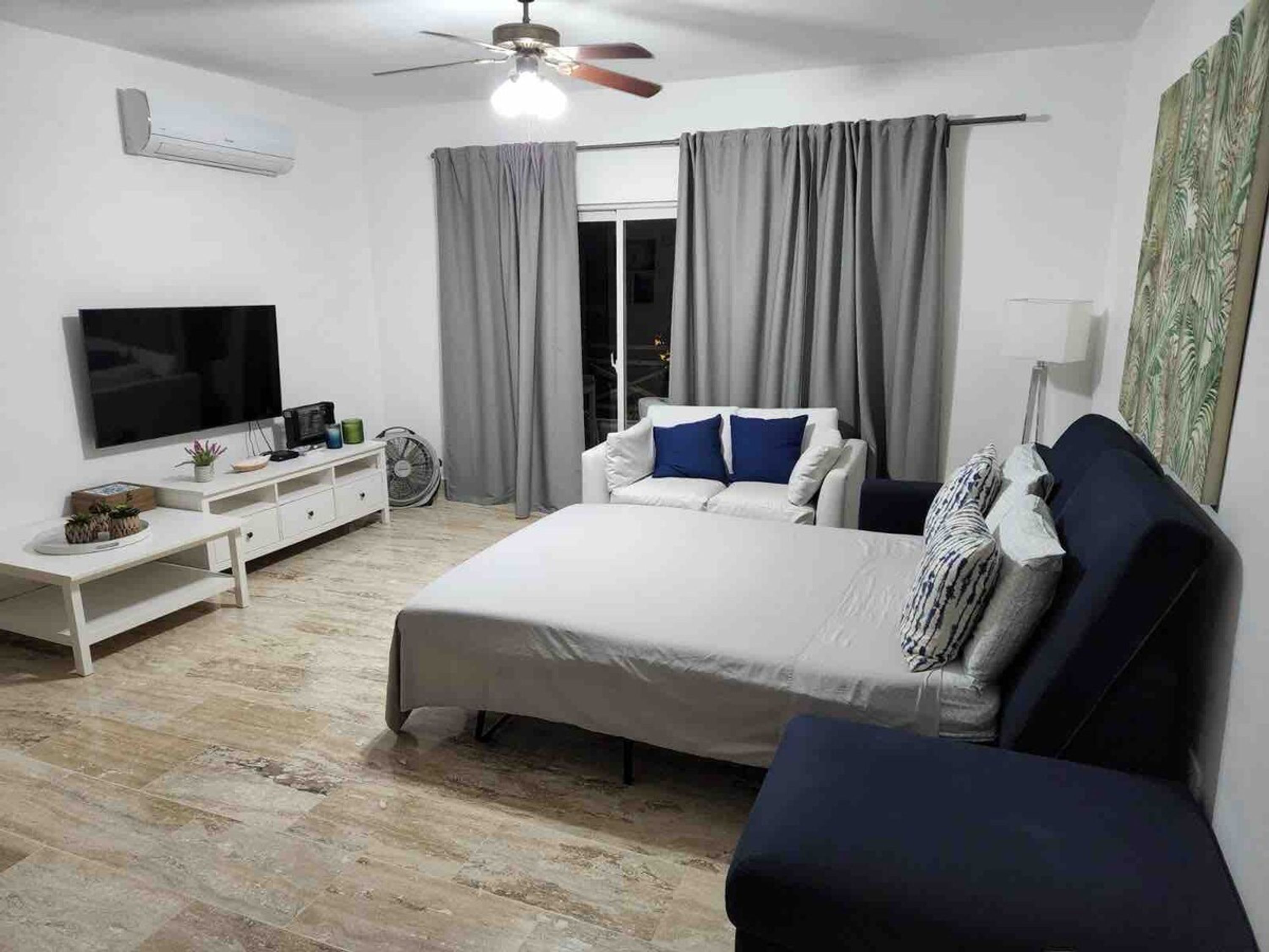 A bedroom with a bed, a TV, a desk, and a ceiling fan.
