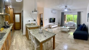 Une cuisine moderne avec des comptoirs en granit, un coin repas avec une table en marbre, un salon avec un canapé et un téléviseur, et un ventilateur de plafond.