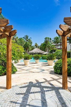 A resort pool area with a thatched umbrella, potted plants, and wooden pergolas. - 3BR Beach Escape Terrenas Pool Family Balcones (Las Terrenas)