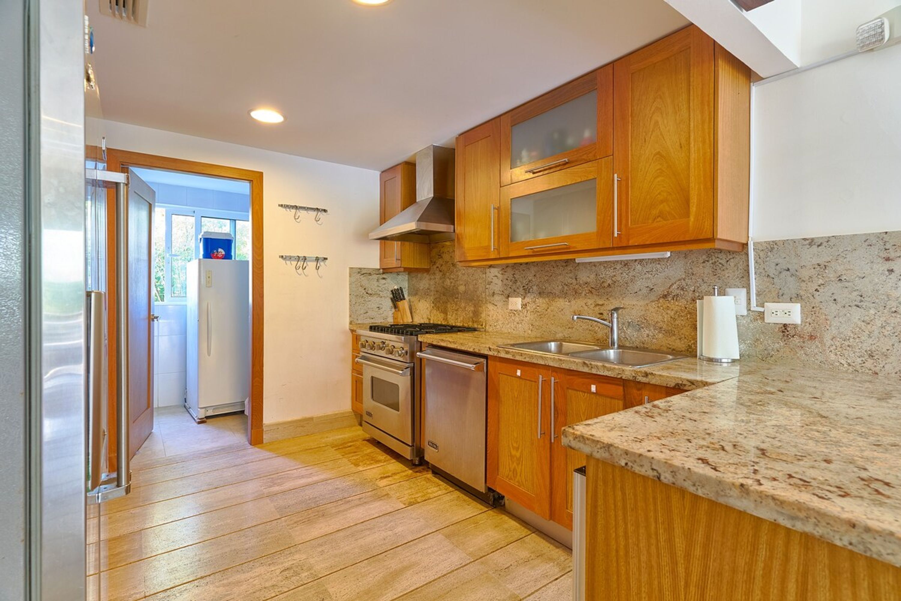 A kitchen with wooden cabinets, a granite countertop, stainless steel appliances, and a view through an open door.