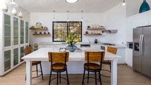 A modern kitchen with white cabinetry, a central island with chairs, pendant lights, and a large window with a view. - Beach Mountain Villa Terrenas Pool BBQ 6BR (Las Terrenas)