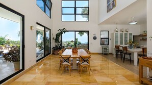 A spacious dining area with a long table and chairs, large windows, and a view of the outdoors. - Beach Mountain Villa Terrenas Pool BBQ 6BR (Las Terrenas)
