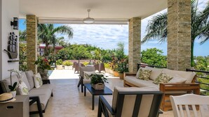 A covered outdoor seating area with a sofa, chairs, and tables, surrounded by potted plants and a view of greenery. - Beach Mountain Villa Terrenas Pool BBQ 6BR (Las Terrenas)
