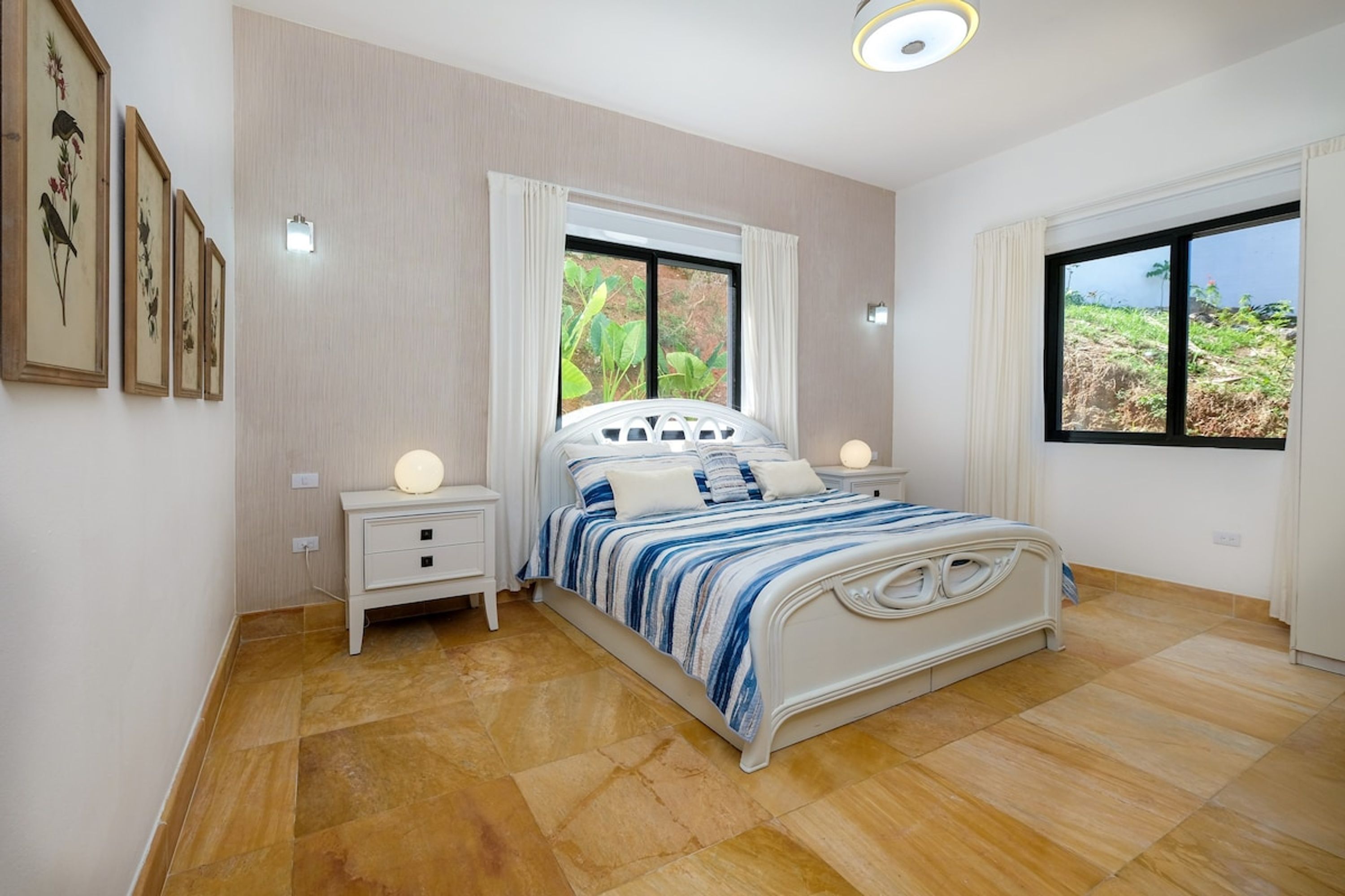 A bedroom with a bed, bedside tables, a window with curtains, and framed artwork on the wall.