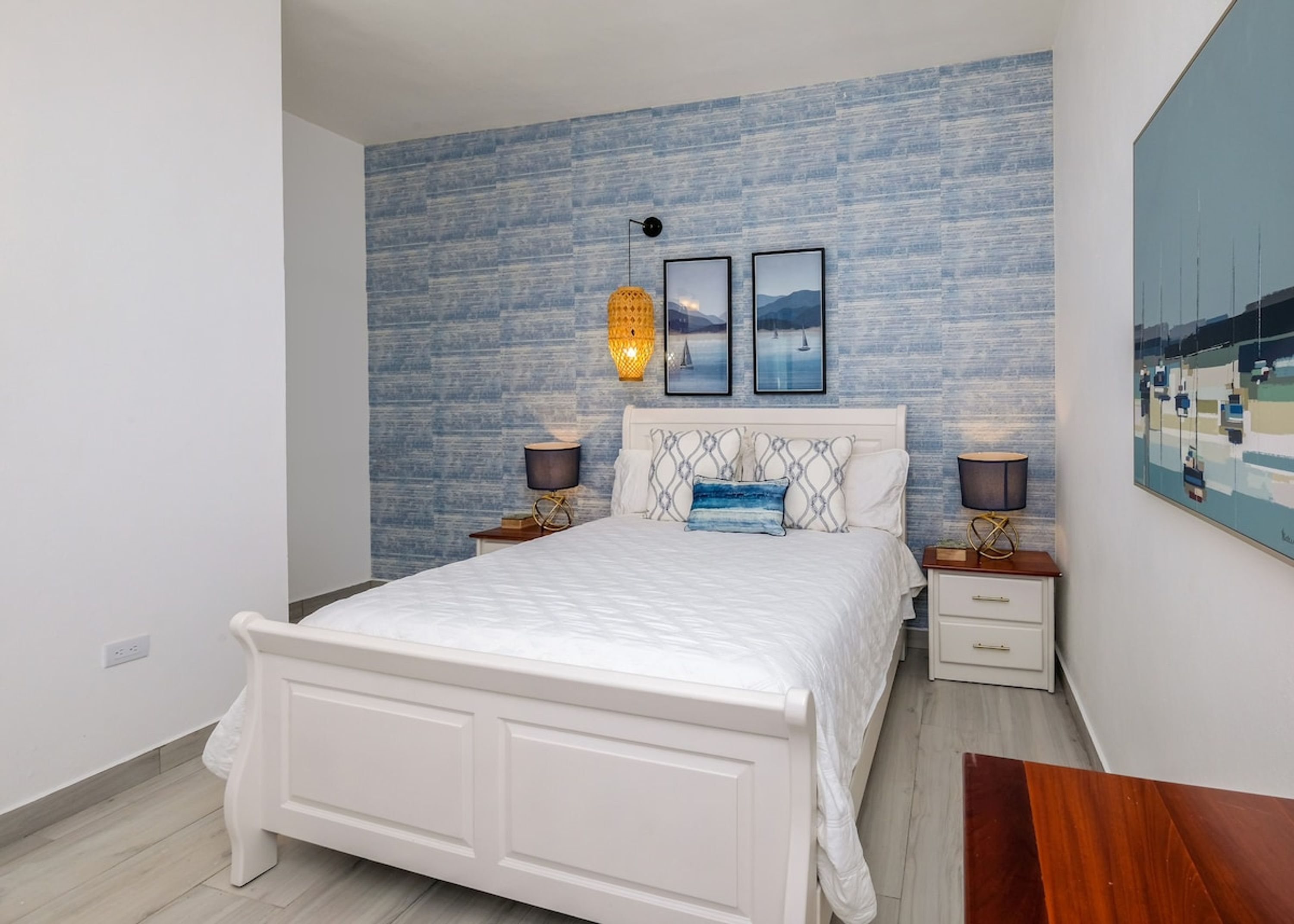 Un dormitorio con una cama, dos mesitas de noche, una lámpara de pared y cuadros enmarcados.