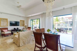 A hotel room with a dining area, a TV, a ceiling fan, and large windows with a view of the outside.