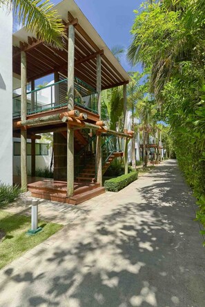 A modern building with a covered outdoor area, a staircase, and a pathway lined with greenery.