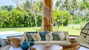 Un área de descanso al aire libre con estilo tropical, que presenta un pilar de madera, techo tejido y vistas a exuberante follaje.