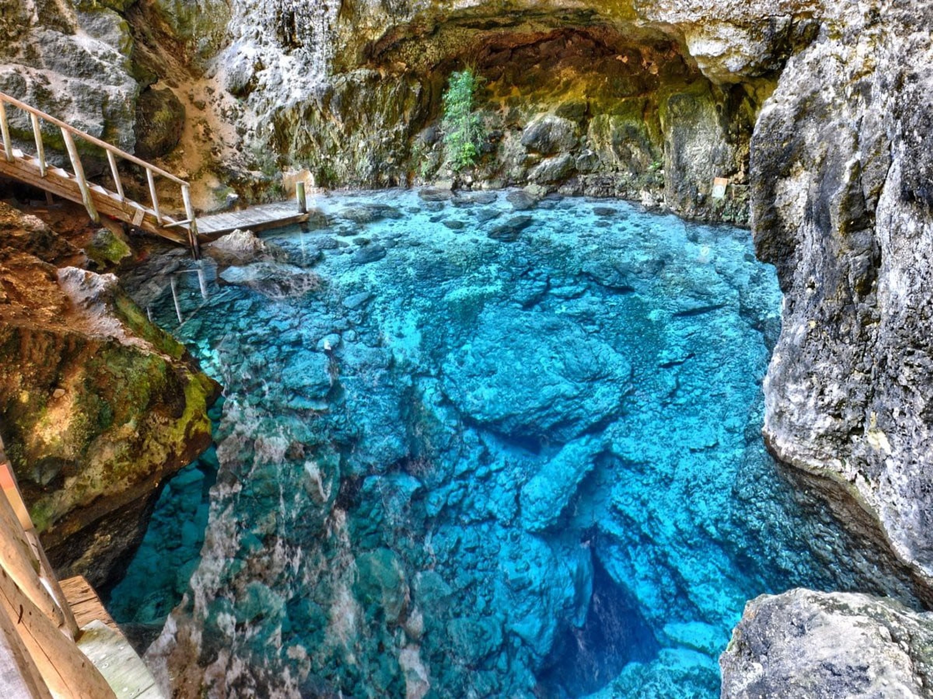 A natural pool with clear blue water surrounded by rocky terrain.